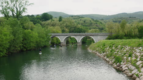 Beautiful-river-side-drone-shot-with-green-nature-and-a-big-arch-bridge-for-cars