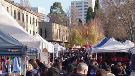 Tourists-and-locals-wandering-stalls-that-line-streets-of-iconic-Salamanca-Market-in-Hobart,-Tasmania,-shopping-for-gifts,-scarf,-hat-on-sunny-winter-day