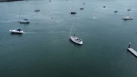 Aerial-view-following-luxury-sailboat-leaving-harbour-and-travelling-along-scenic-river-estuary
