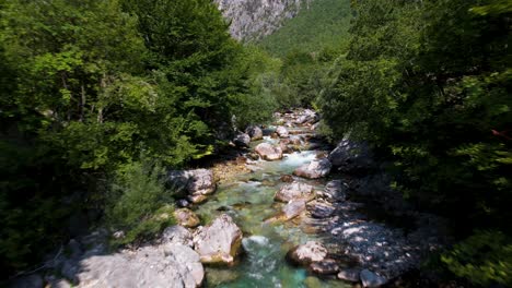 Mountain-river-with-clean-water-streaming-across-cliffs-and-trees-in-valley-of-Valbone,-Albania