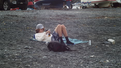 Young-Male-Relaxing-And-Using-Smartphone-Outdoor-Near-Porthallow-Fishing-Village-In-Cornwall,-England,-United-Kingdom---wide-shot
