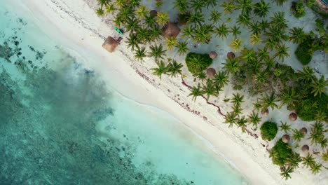Spinning-aerial-bird's-eye-drone-view-of-a-beautiful-tropical-vacation-beach-with-crystal-clear-blue-water,-white-sand,-palm-trees,-and-a-kayak-and-lifeguard-tower-in-Riviera-Maya,-Mexico-near-Cancun