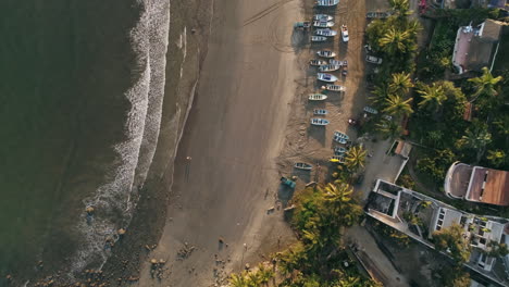 Top-down-aerial-along-beach-over-fishing-boats-sitting-on-sand-in-morning,-4K