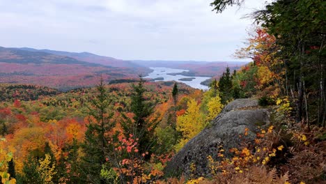 Panoramic-shot-overlooking-a-colorful-dense-forest-of-red-green-and-yellow-trees-and-a-large-lake-below-in-the-distance