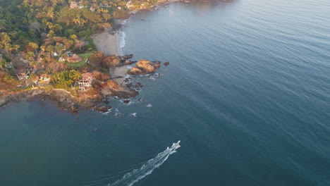 Aerial-of-small-boat-speeding-around-rocky-point-with-luxury-villas,-4K