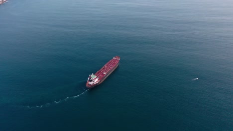 Aerial-flying-above-red-freighter-cargo-ship-at-calm-blue-sea-at-day