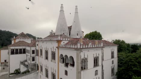 Filmische-Touristenaufnahme-Mit-Einem-Schwarm-Vögel,-Die-Um-Den-Stadtpalast-Von-Sintra,-Portugal,-Herumfliegen