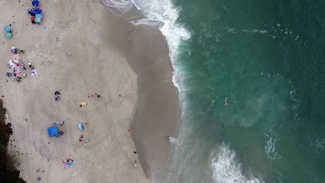 Waves-Washing-On-Beach-Shore-With-Tourists-Relaxing-On-Beach,-Top-Down-Bird-Eye-View