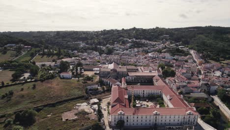 Aerial-pull-out-shot-away-Alcobaça-monastery-complex-overlooking-at-cityscape-and-distance-landscape