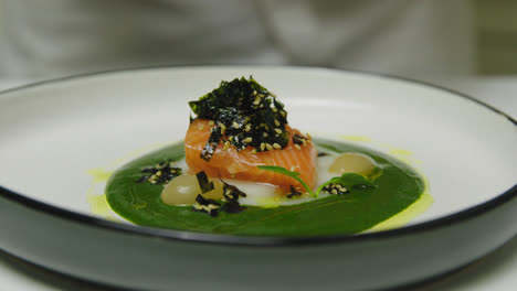 Close-up-shot-of-professional-chef-in-luxury-restaurant-adding-greens-on-fancy-served-salmon-plate