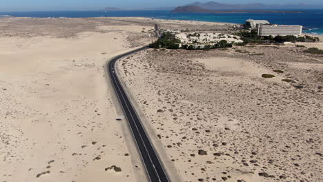 Drone-dolly-in-shot-on-the-road,-seeing-a-hotel-complex-on-the-beach-of-Corralejo,-Fuerteventura,-Canary-Islands