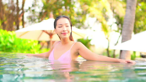 Mujer-Asiática-Feliz-Sonriente-En-Un-Bikini-De-Color-Rosa-Dentro-De-La-Piscina-Mirando-A-Un-Lado