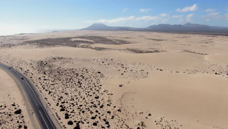 drone-shot-over-road-and-infinite-sand-of-corralejo-beach,-Fuerteventura,-canary-islands