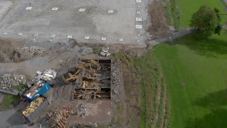 Sitio-De-Construcción-Con-Excavadora,-Reverso-Aéreo-Que-Revela-El-Paisaje-Urbano-En-El-País-Nórdico