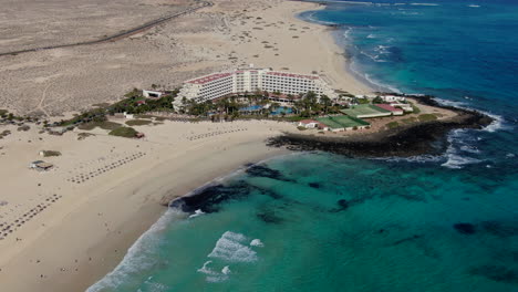 drone-shot-in-orbit-over-hotel-complex-in-and-over-the-sea,-corralejo-beach,-Fuerteventura,-canary-islands
