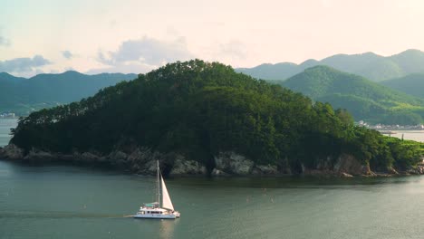 Small-White-Boat-Sailing-By-The-Shore-Of-An-Island-in-Geonje-City-South-Korea---wide-shot