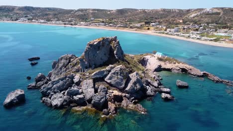 Cinematic-aerial-shot-of-a-rock-formation-in-a-paradisiacal-greek-island-with-a-small-church-on-it