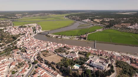 Aerial-pan-shot-of-estuary-side-agriculture-rice-paddy-fields,-townscape-of-Alcacer-do-Sol,-Portugal