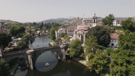 Scenic-aerial-ascending-shot-of-historical-bridge-over-Tamega-river-and-riverside-Sao-Goncalo-church