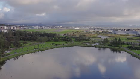 Lake-Tjörnin-with-reflection-of-clouds-on-surface,-distant-Reykjavik-airport