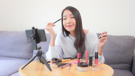 Asian-female-blogger-applying-makeup-mascara-with-a-brush,-beauty-cosmetics-concept-makeup-YouTuber-recording-video-on-a-smartphone