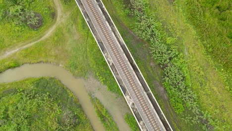 Descending-aerial-footage-revealing-dirt-roads,-canal-filled-with-rain-water-in-this-marshy-land,-elevated-railway