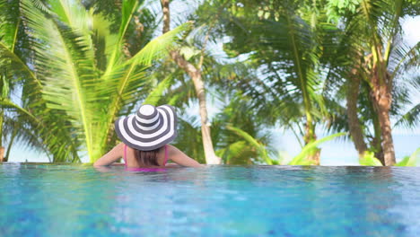 Lonely-Woman-in-Infinity-Swimming-Pool-on-Tropical-Destination,-Back-View-of-Female-in-Floppy-Hat-Looking-at-Exotic-Vegetation,-Full-Frame