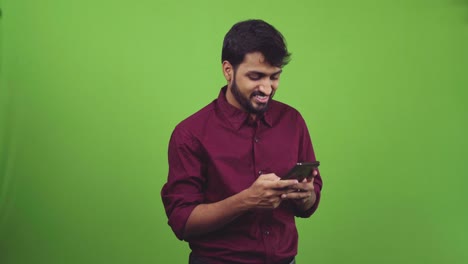 Asian-man-clad-in-burgundy-colored-shirt-smiling-and-texting-in-a-green-screen-shoot