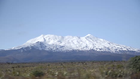 Driving-by-Mount-Ruapehu-covered-in-white-snow,-bush-passing-by-in-front,-motion-blur