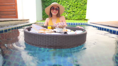Young-Asian-woman-pushes-tray-floating-on-pool-water-with-breakfast-food