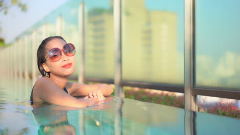 Junge-Asiatin-Mit-Großer-Sonnenbrille,-Die-Sich-Im-Dachpool-Des-Hotels-Entspannt-Und-In-Die-Kamera-Schaut