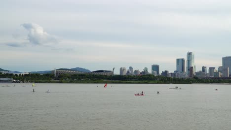 Windsurfing-And-Kayaking-At-Han-River-With-Olympic-Stadium-And-Trade-Tower-In-Background-In-Seoul,-South-Korea