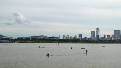 Paddle-Surf-En-El-Río-Han-Con-Estadio-Olímpico-Y-Torre-De-Comercio-En-Seúl,-Corea-Del-Sur