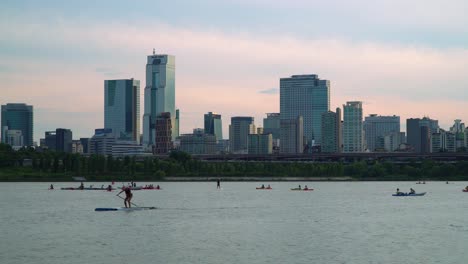 Standup-Paddleboarding-And-Kayaking-At-Han-River-With-Trade-Tower-And-Skyscrapers-In-Background-In-Seoul,-South-Korea