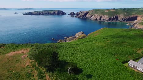 Drone-flying-towards-revealing-a-big-isolated-house-in-the-middle-of-a-green-landscape-in-the-Island-of-Sark,-Channel-Islands