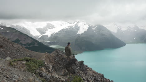 Hombre-En-Una-Montaña-Escarpada-Admirando-La-Pintoresca-Vista-Del-Lago-Garibaldi-En-El-Parque-Provincial-Garibaldi,-Bc,-Canadá