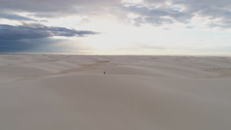 Aerial-view-of-person-walking-in-vast-white-sand-dune-field-at-sunrise,-4K