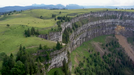 Descending-drone-shot-of-Creux-du-Van-in-Switzerland,-located-at-the-border-of-the-cantons-of-Neuenburg-and-Vaud