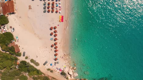 Overhead-aerial-flight-over-turquoise-waters-summer-beach-with-umbrellas