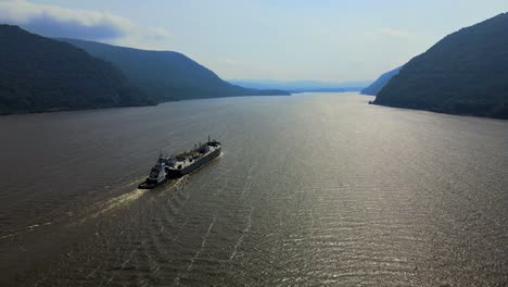 Aerial-drone-video-footage-of-a-large-cargo-ship-on-the-Hudson-River-in-New-York's-Hudson-Valley,-going-through-the-Hudson-Highlands-on-a-sunny-day-in-late-summer-or-early-fall