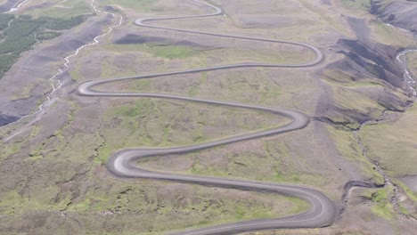 Winding-dirt-road-going-downhill-into-valley-of-lake-Lagarfljót,-Iceland,-Aerial