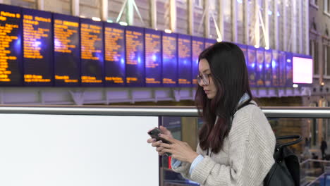 Young-student-tourist-checks-her-phone-while-waiting-for-a-train-at-Kings-Cross-Station,-London,-England