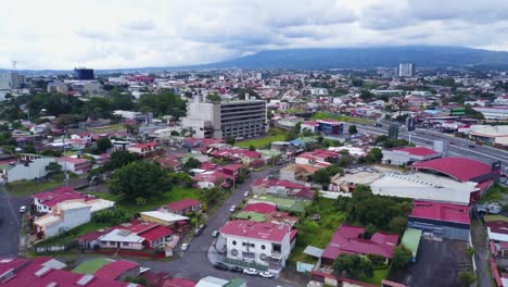 Aerial-drone-shot-showing-the-suburbs-of-San-Jose,-Costa-Rica,-with-houses,-commercial-buildings,-cars,-green-grass