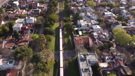 Aerial-view-of-red-train-passing-by-residential-housing-in-Buenos-Aires,-Argentina