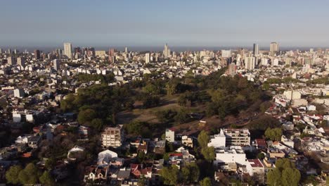 Aerial-shot-of-idyllic-Saavedra-Park-surrounded-by-giant-skyscraper-city-of-Buenos-Aires-during-sunset