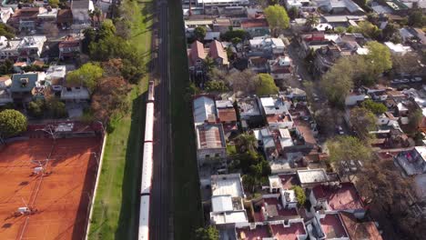 Aerial-view-of-red-train-passing-by-club-in-Buenos-Aires,-Argentina