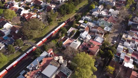 Public-train-in-red-color-riding-on-tracks-in-rural-suburb-of-Buenos-Aires---Aerial-tracking-shot