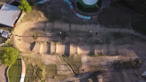 Aerial-top-down-shot-of-bmx-cyclist-riding-and-practicing-at-sandy-dirty-race-track-during-sunset-in-Buenos-Aires,Argentina