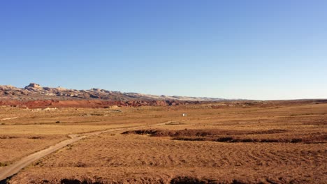 Atemberaubende-Drohne-Aus-Der-Luft,-Die-Eine-Linke-Aufnahme-Von-Autos-Zeigt,-Die-Eine-Kleine-Wüstenpiste-Mit-Orangefarbenem-Schmutz,-Weißen-Und-Roten-Felsformationen-Und-Einem-Blauen-Sommerhimmel-In-Utah-In-Der-Nähe-Des-Goblin-Valley-State-Park-Hinunterfahren