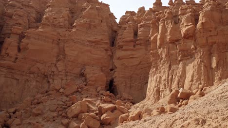 Beautiful-tilting-up-shot-revealing-the-large-opening-entrance-of-the-Goblin's-Lair-cave-in-the-Utah-State-Park-Goblin-Valley-on-a-hike-on-a-warm-sunny-summer-day-surrounded-by-red-rocks